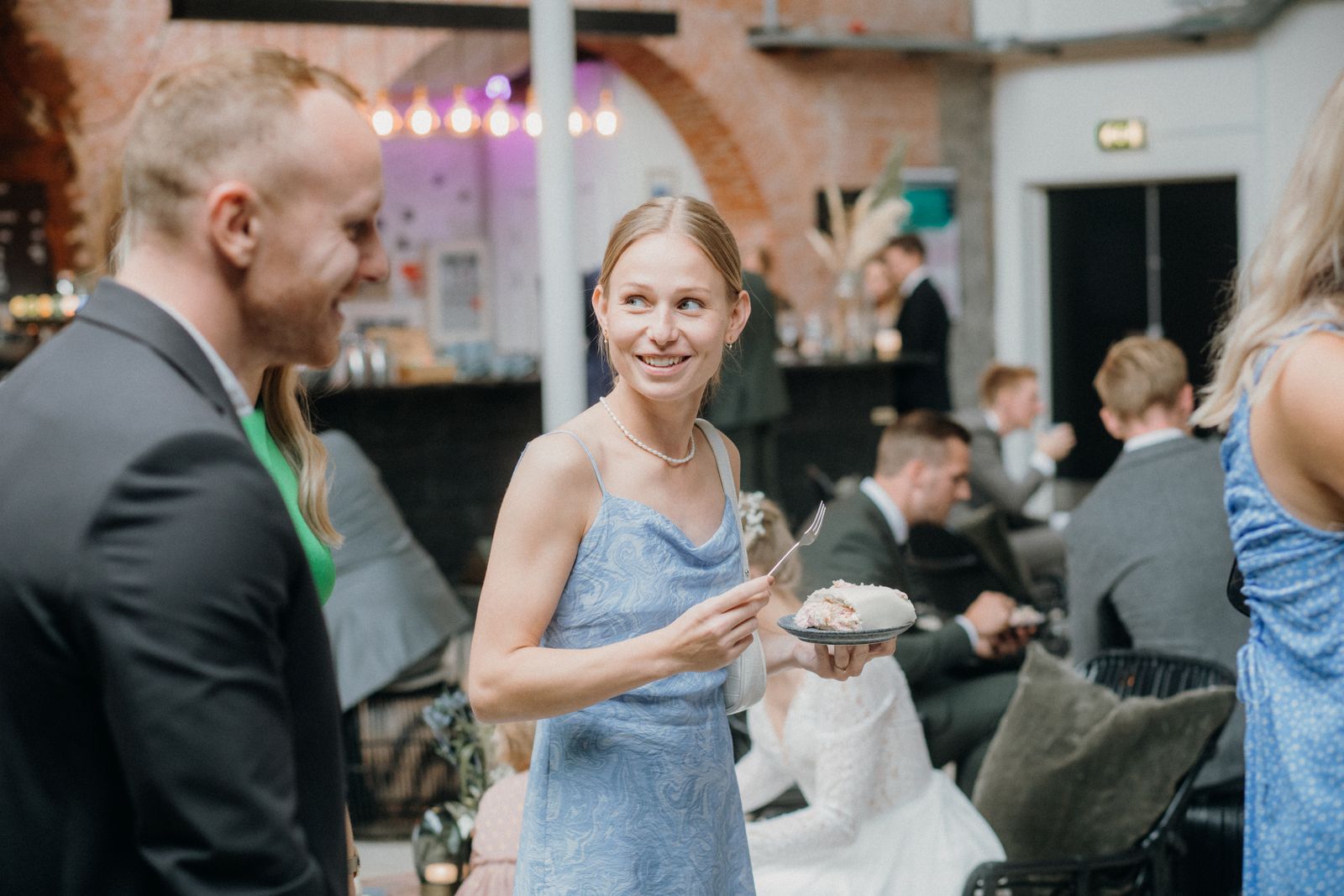 Fotode jagamine külalistele üritusel Peoline seltskond pulmapeol vanas tellisseinaga saalis, külalised vestlevad ja naeravad